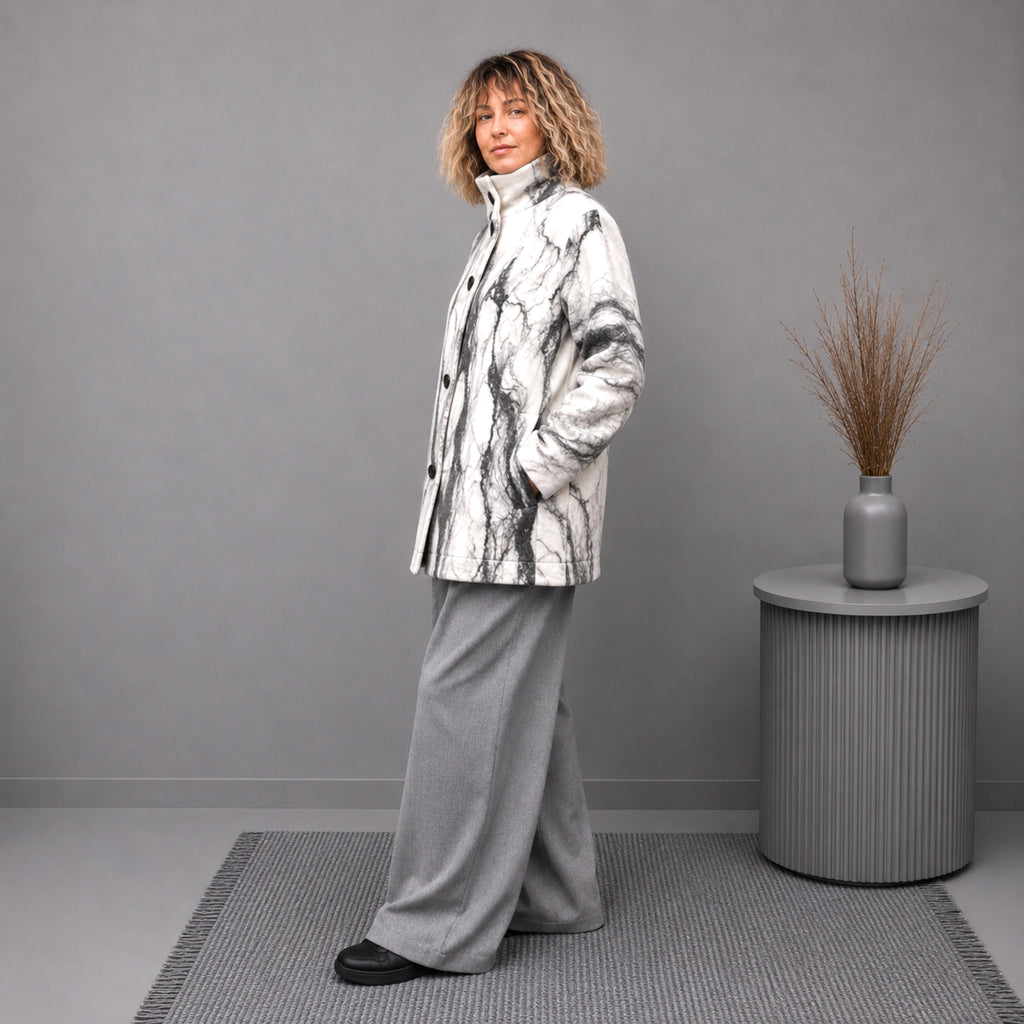 A woman stands in a studio wearing a white and gray merino wool coat