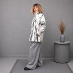 A woman stands in a studio wearing a white and gray merino wool coat