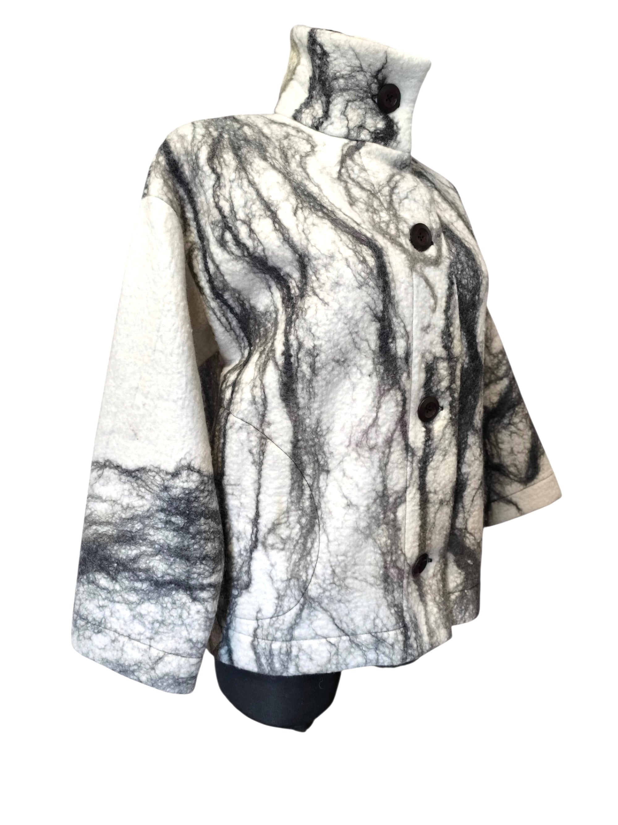 A high-neck, long-sleeve coat with a black and white marbled or crackled pattern, displayed on a black mannequin torso against a white background.